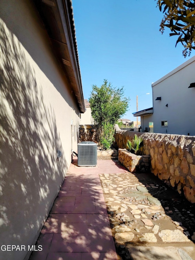 view of side of property with a patio area, stucco siding, fence, and central AC