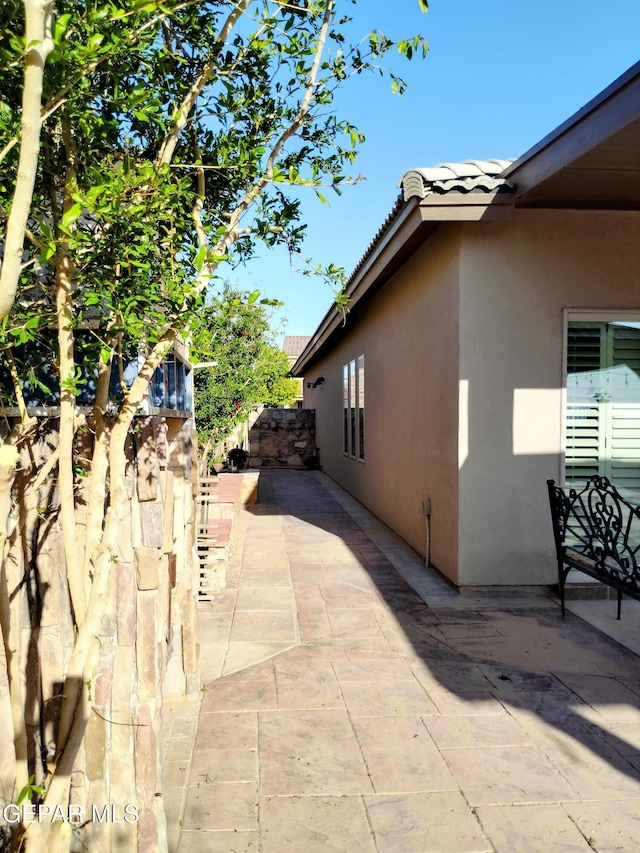view of side of home with a patio, stucco siding, a tiled roof, and fence