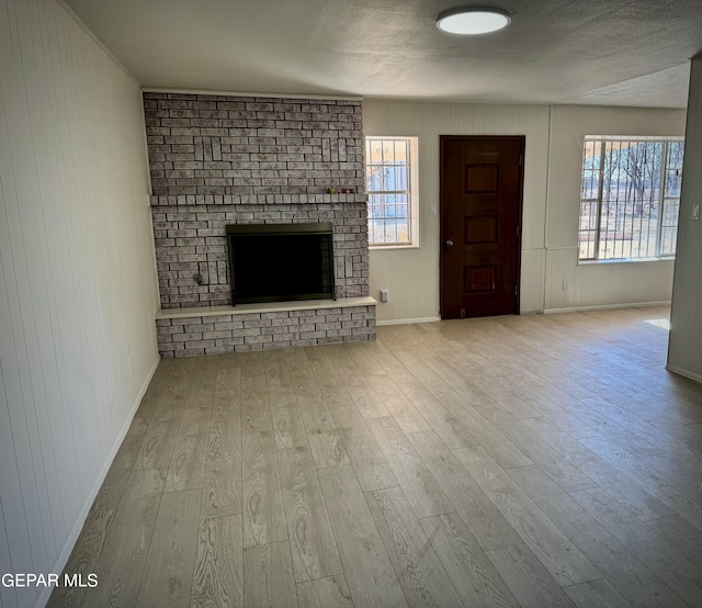 unfurnished living room with a brick fireplace, light hardwood / wood-style flooring, and wood walls