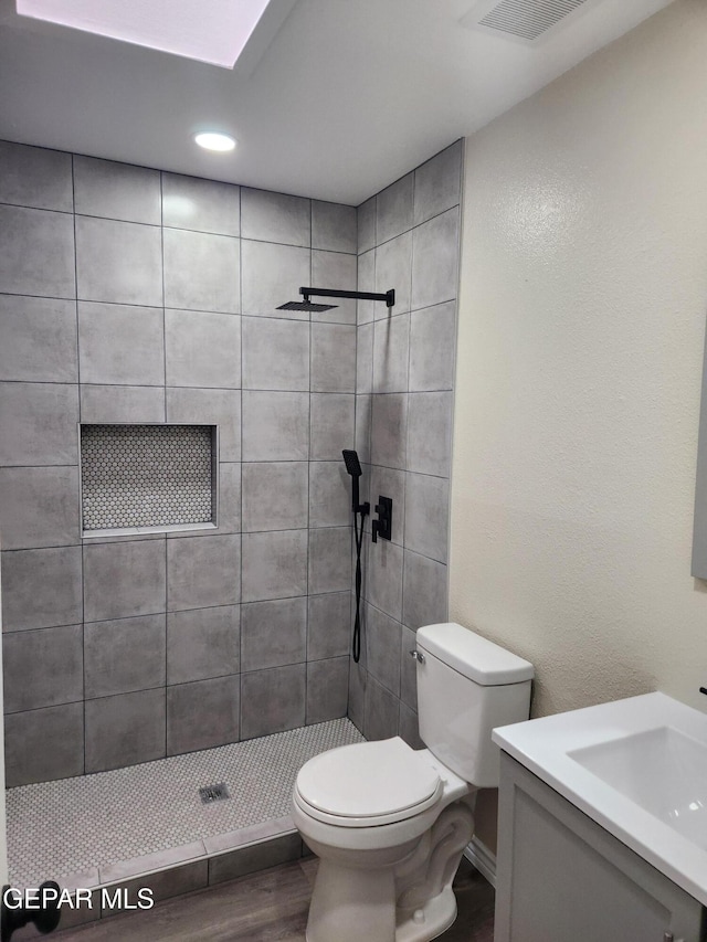 bathroom featuring hardwood / wood-style floors, vanity, a tile shower, and toilet