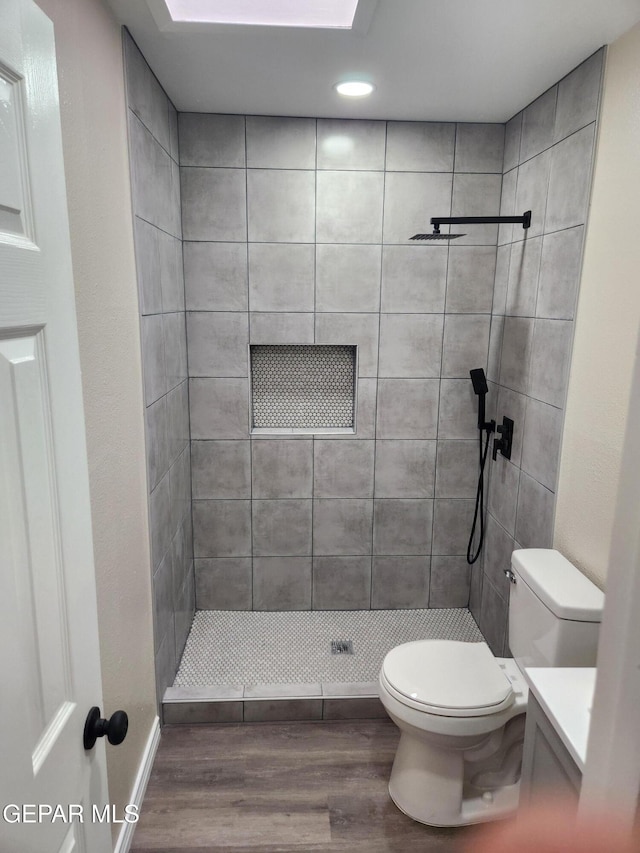 bathroom with wood-type flooring, tiled shower, vanity, and toilet