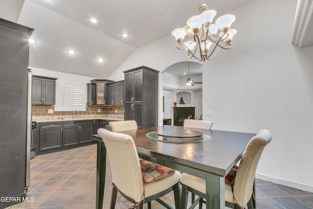 tiled dining room with sink, ceiling fan with notable chandelier, and lofted ceiling