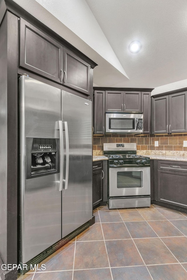 kitchen with dark brown cabinets, stainless steel appliances, light stone countertops, and vaulted ceiling