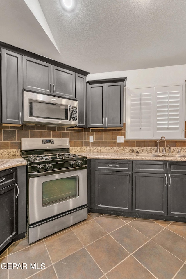 kitchen with light stone countertops, a textured ceiling, appliances with stainless steel finishes, dark tile patterned floors, and tasteful backsplash