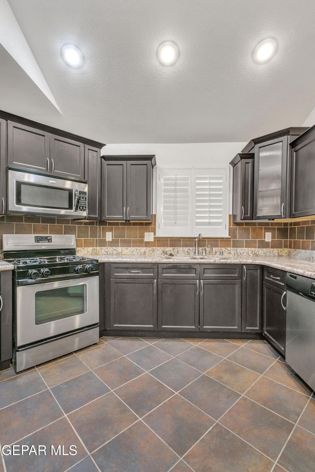 kitchen featuring light stone countertops, vaulted ceiling, appliances with stainless steel finishes, and tasteful backsplash