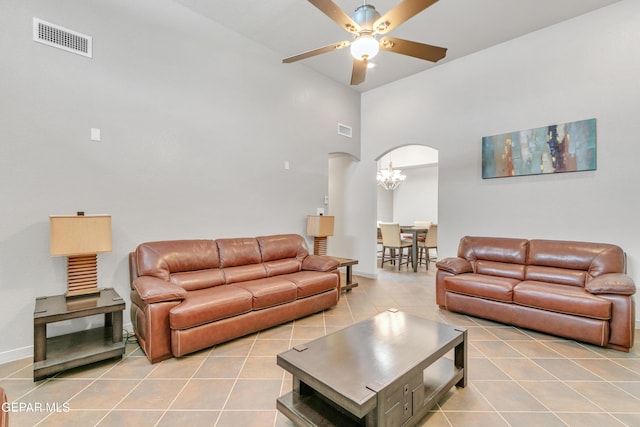 living room with a towering ceiling, ceiling fan with notable chandelier, and light tile patterned flooring