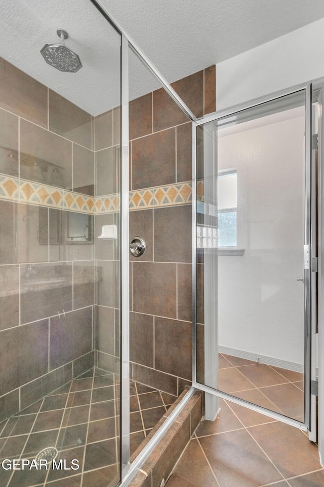 bathroom with a textured ceiling, tiled shower, and tile patterned flooring