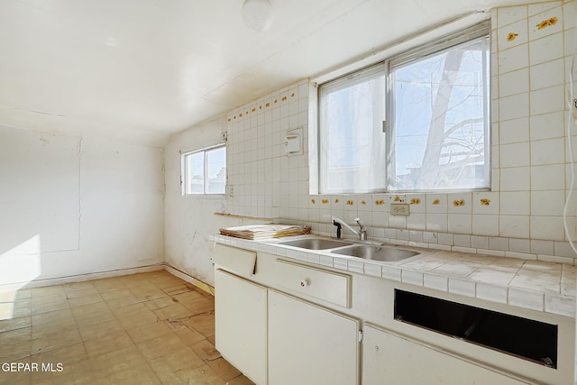 kitchen with sink, white cabinetry, tile countertops, tile walls, and backsplash