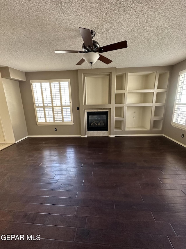 unfurnished living room with a textured ceiling, ceiling fan, built in features, and dark hardwood / wood-style floors