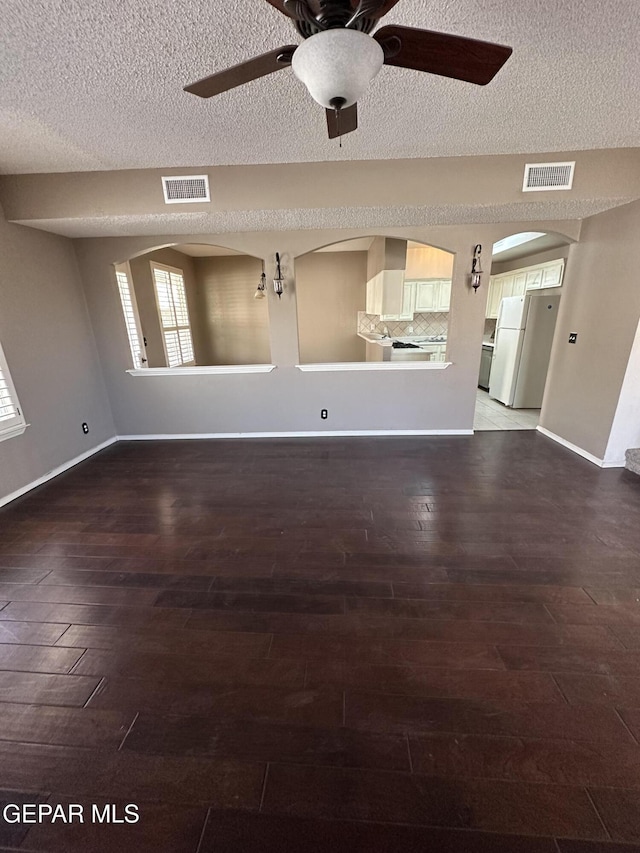 unfurnished living room featuring a textured ceiling, ceiling fan, and dark hardwood / wood-style floors