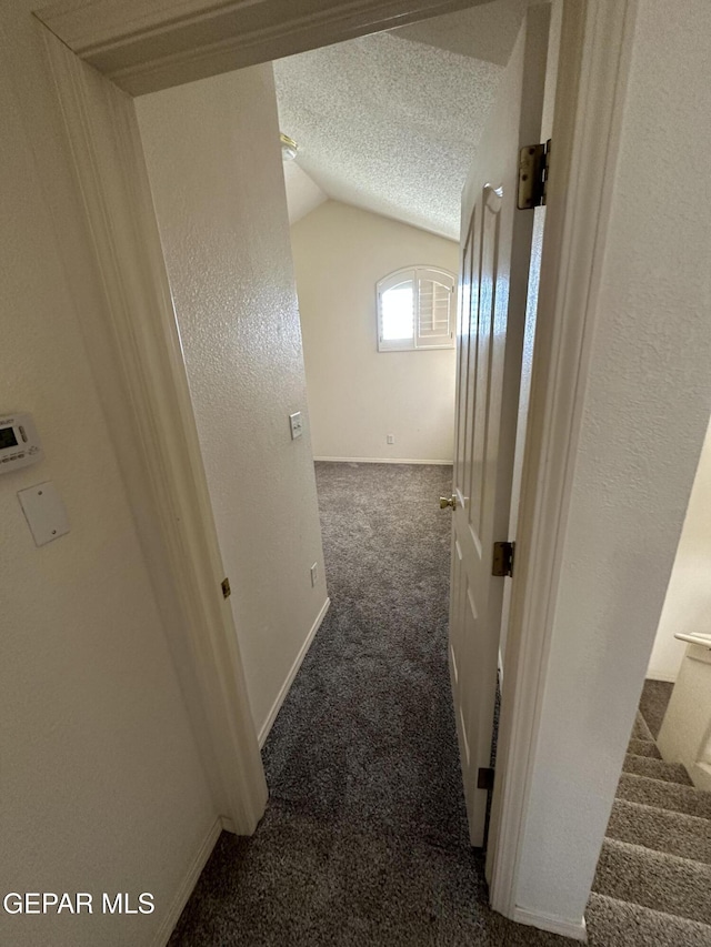 corridor featuring a textured ceiling, vaulted ceiling, and dark carpet