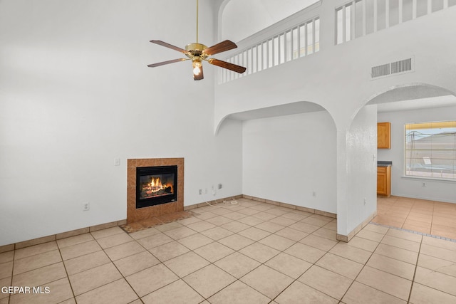 unfurnished living room featuring a towering ceiling, ceiling fan, light tile patterned floors, and a tiled fireplace