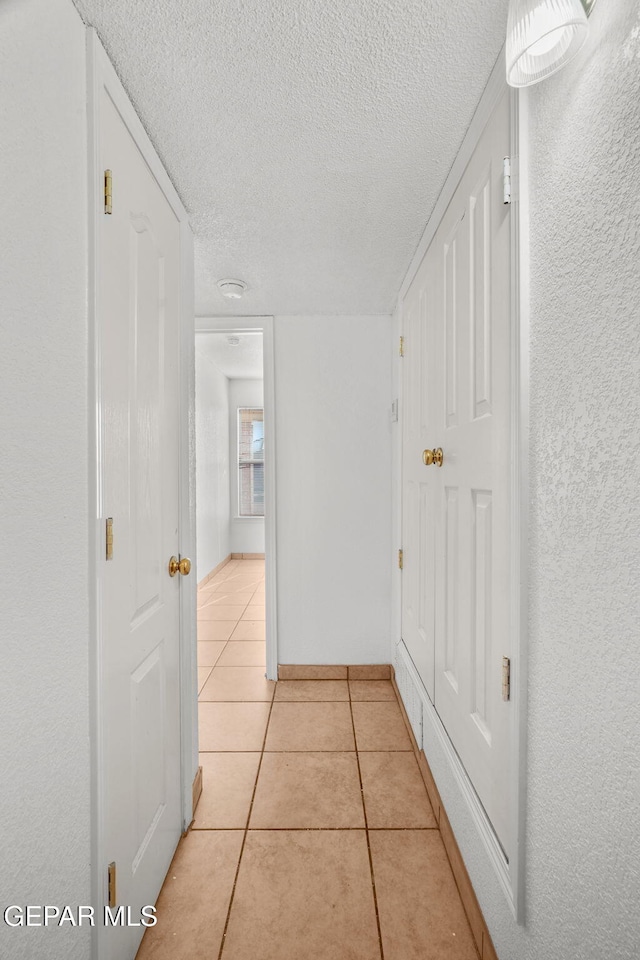 corridor with a textured ceiling and light tile patterned flooring