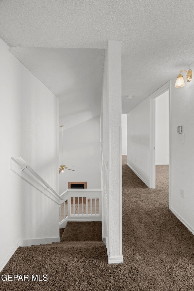 stairway with ceiling fan, a textured ceiling, and carpet