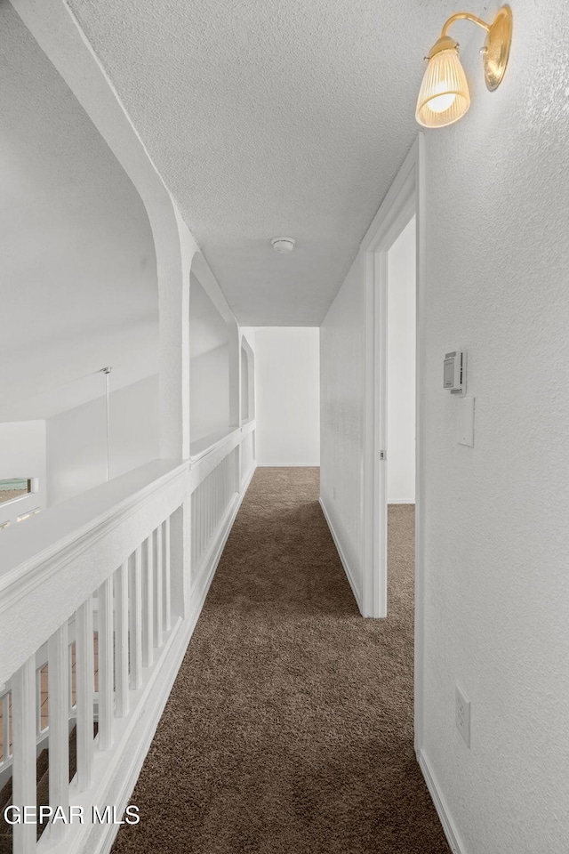 hall with dark colored carpet and a textured ceiling