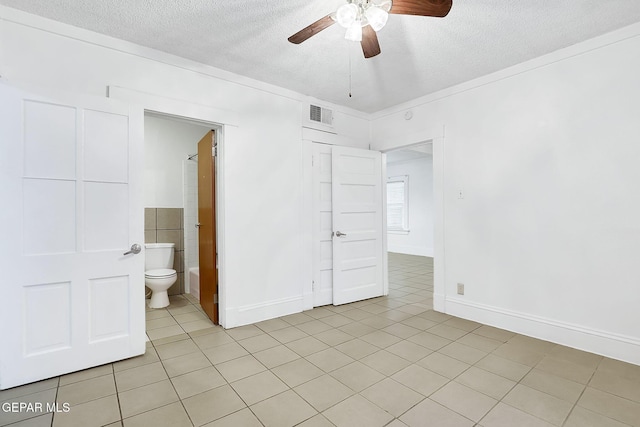 unfurnished bedroom with connected bathroom, a textured ceiling, ceiling fan, and light tile patterned floors