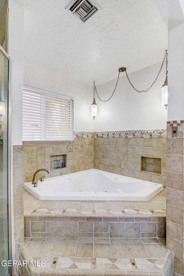 bathroom featuring a textured ceiling and tiled tub