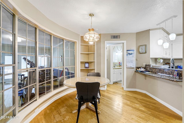 dining room with light wood-type flooring, an inviting chandelier, and a textured ceiling