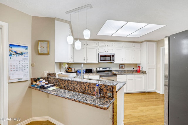 kitchen featuring appliances with stainless steel finishes, white cabinetry, dark stone countertops, decorative light fixtures, and kitchen peninsula