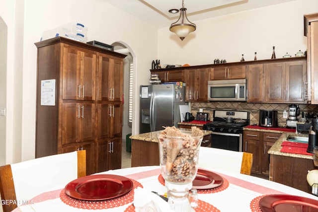 kitchen with appliances with stainless steel finishes, sink, decorative backsplash, hanging light fixtures, and light stone counters