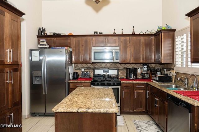 kitchen with tasteful backsplash, a center island, light tile patterned floors, appliances with stainless steel finishes, and light stone countertops