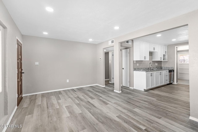 kitchen featuring light stone countertops, sink, white cabinets, and light wood-type flooring