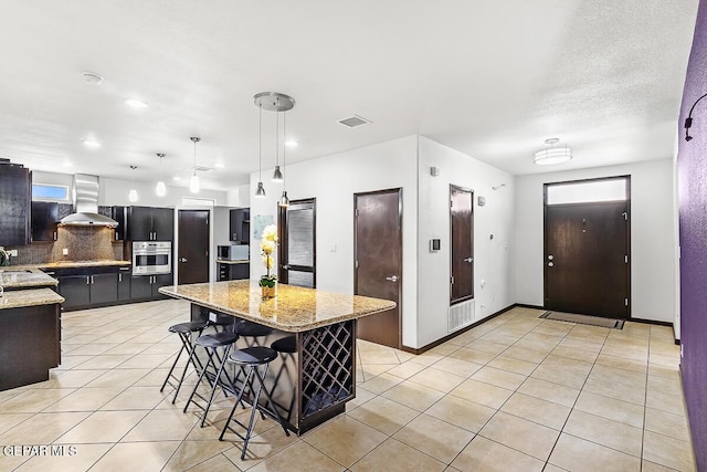 kitchen featuring a kitchen island, pendant lighting, a kitchen breakfast bar, stainless steel appliances, and wall chimney exhaust hood