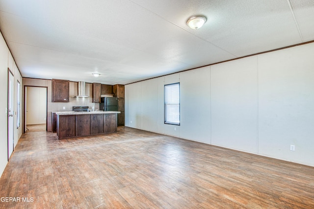 kitchen with black fridge, a center island, hardwood / wood-style flooring, wall chimney range hood, and stove