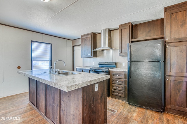 kitchen featuring sink, a kitchen island with sink, black appliances, wall chimney exhaust hood, and light wood-type flooring