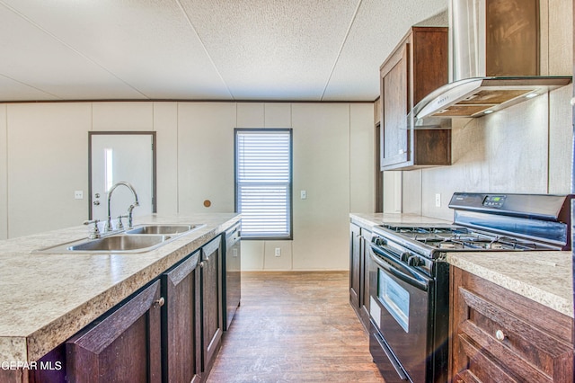 kitchen featuring sink, stainless steel dishwasher, black gas stove, an island with sink, and wall chimney range hood