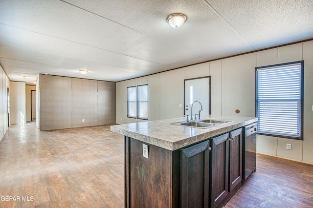 kitchen with dark brown cabinetry, sink, a center island with sink, stainless steel dishwasher, and hardwood / wood-style floors