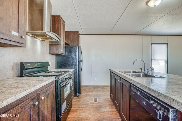 kitchen with wall chimney range hood, sink, wood-type flooring, black appliances, and a textured ceiling