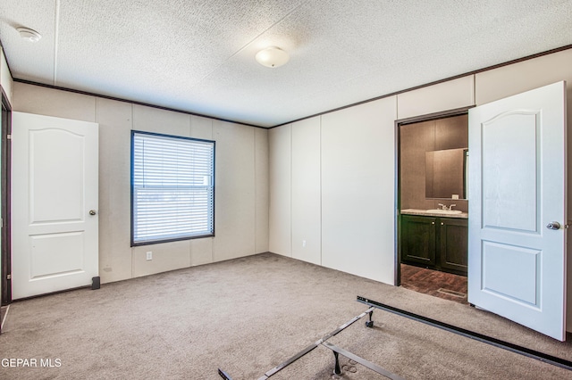 unfurnished bedroom with ensuite bathroom, carpet flooring, sink, and a textured ceiling