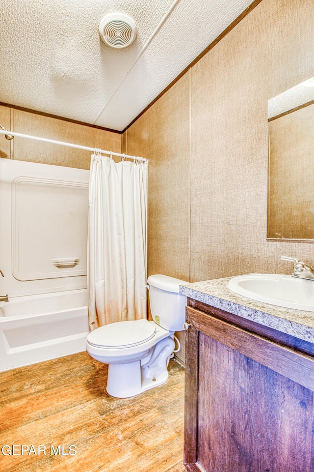 full bathroom featuring hardwood / wood-style floors, vanity, shower / tub combo, toilet, and a textured ceiling