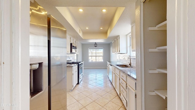 kitchen featuring sink, light stone counters, a raised ceiling, stainless steel appliances, and decorative backsplash