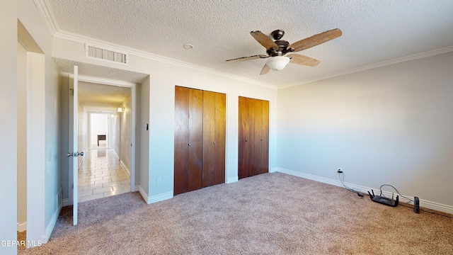 unfurnished bedroom featuring crown molding, a textured ceiling, multiple closets, carpet flooring, and ceiling fan