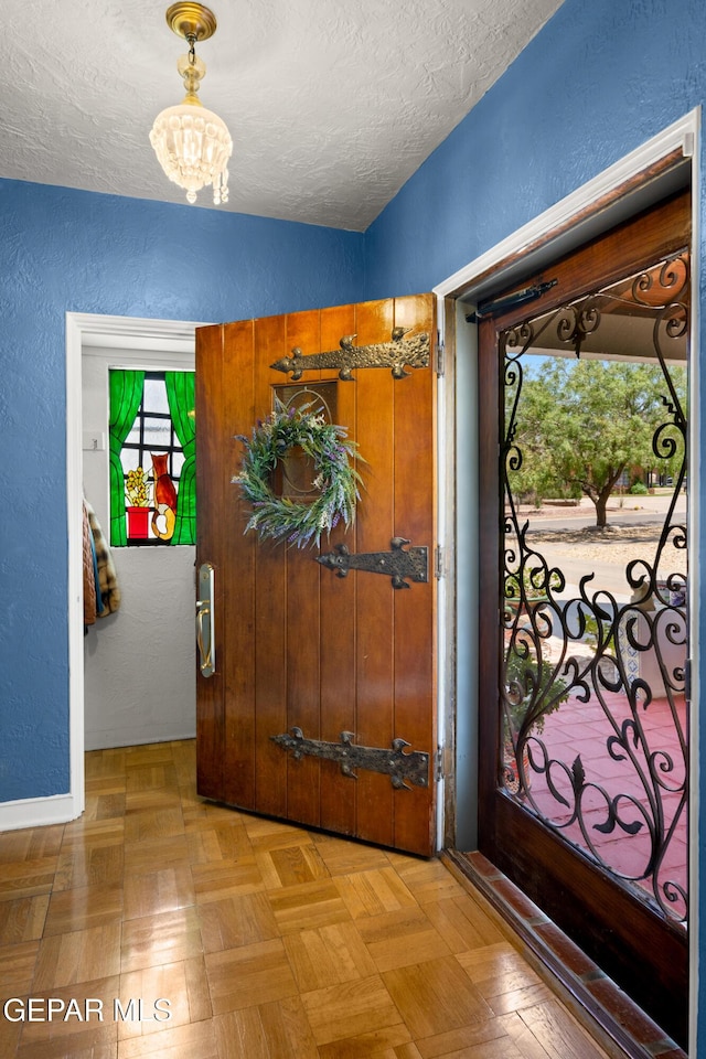 entrance foyer with light parquet floors, a chandelier, and a textured ceiling