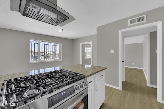 kitchen with stainless steel gas stove, a textured ceiling, light wood-type flooring, light stone countertops, and white cabinets