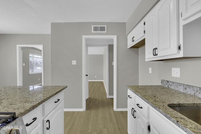 kitchen with white cabinetry, light stone countertops, stove, and light wood-type flooring