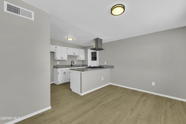 kitchen featuring range hood, stainless steel gas stovetop, white cabinetry, kitchen peninsula, and a textured ceiling