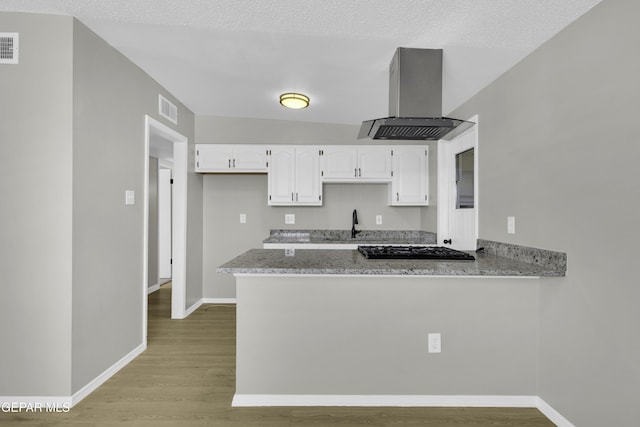 kitchen featuring white cabinetry, island exhaust hood, stainless steel gas cooktop, kitchen peninsula, and light stone countertops