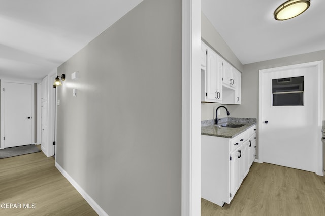 kitchen featuring dark stone countertops, sink, white cabinets, and light wood-type flooring