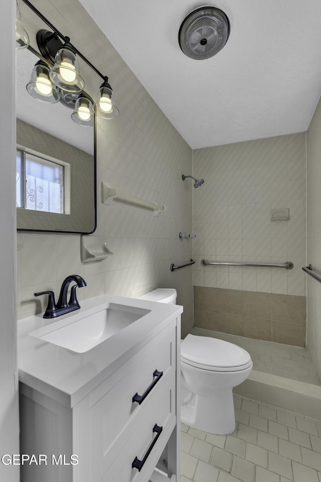 bathroom featuring tiled shower, toilet, tile walls, vanity, and tile patterned flooring