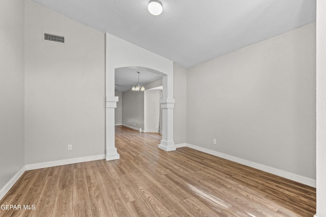 spare room featuring wood-type flooring, a chandelier, and a textured ceiling