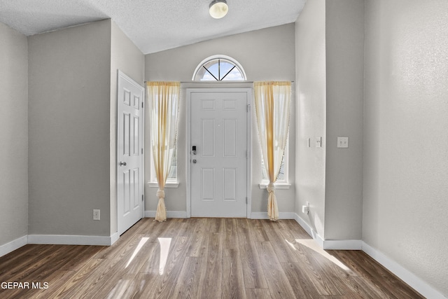 entryway featuring lofted ceiling, wood-type flooring, and a textured ceiling