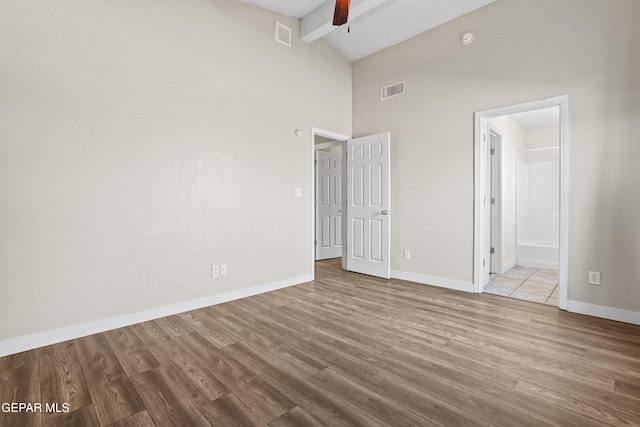 unfurnished bedroom featuring high vaulted ceiling, connected bathroom, beam ceiling, and light hardwood / wood-style floors