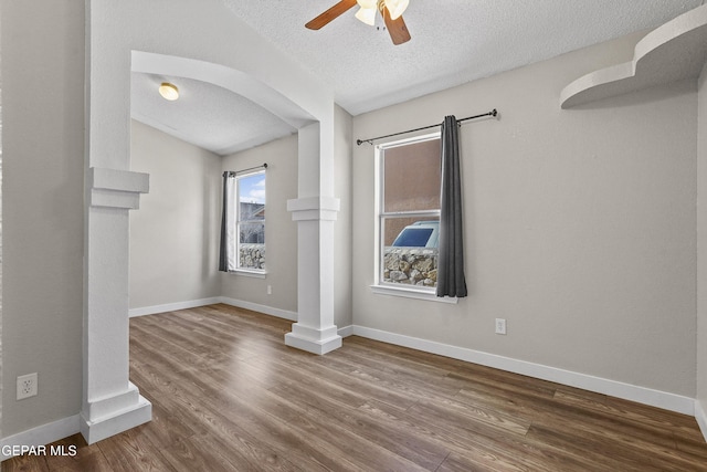 unfurnished room with lofted ceiling, ceiling fan, decorative columns, wood-type flooring, and a textured ceiling