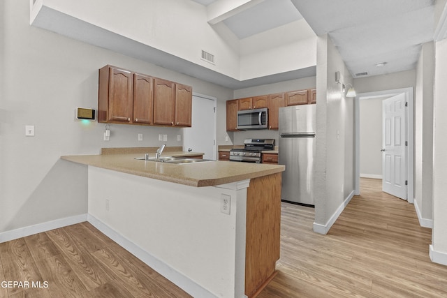 kitchen with sink, a high ceiling, kitchen peninsula, stainless steel appliances, and light hardwood / wood-style flooring