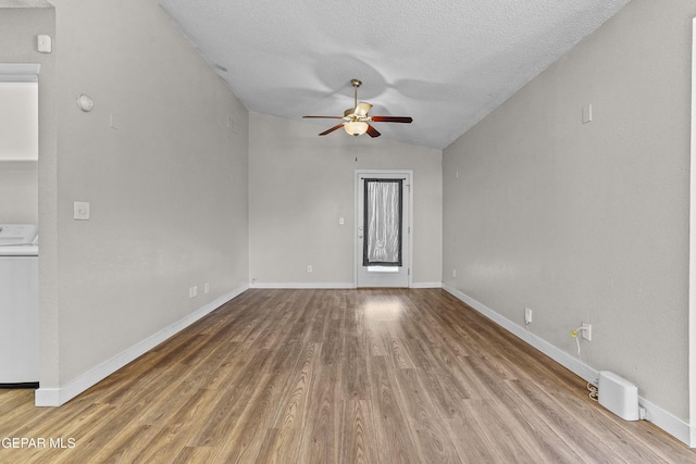 empty room featuring washer / dryer, vaulted ceiling, a textured ceiling, hardwood / wood-style flooring, and ceiling fan