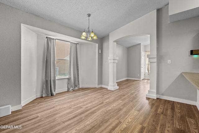 unfurnished dining area with a notable chandelier, a textured ceiling, and light hardwood / wood-style flooring